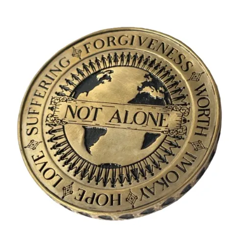 Close-up of a brass coin pendant featuring intricate "Not Alone" globe design and motivational text featuring Ethereal font in use