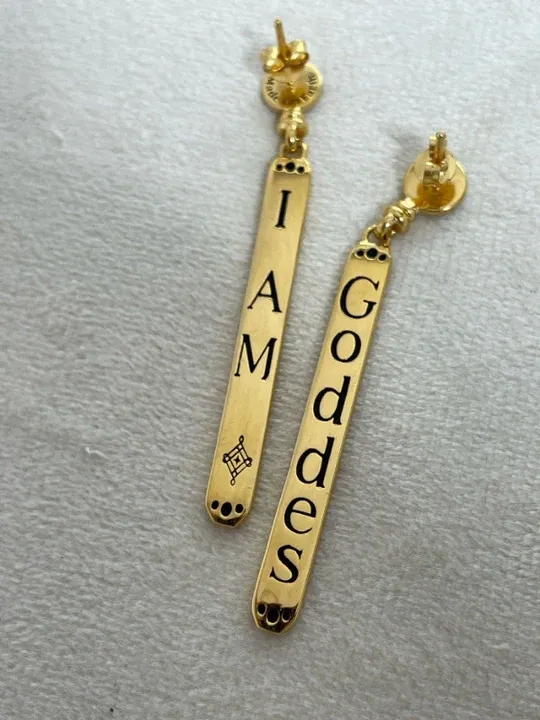 Pair of long gold bar earrings engraved with the words "I AM" and "GODDESS" featuring Ethereal font in use