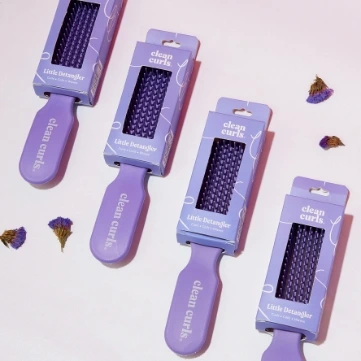 Four purple detangling brushes arranged diagonally on a clean white surface featuring Asikue font in use