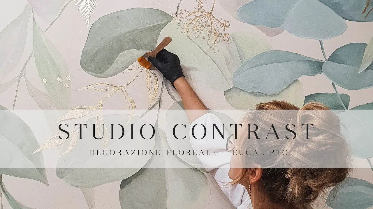 Close-up of an artist's hand adding gold leaf details to a large eucalyptus leaf mural featuring Ethereal font in use